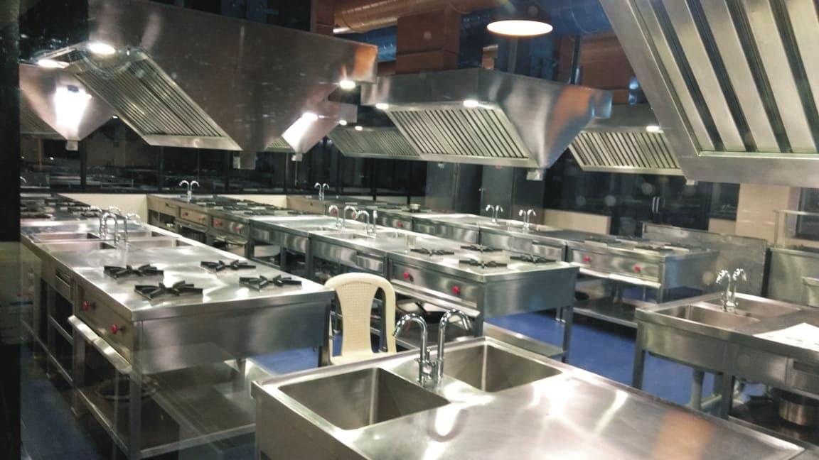 Stainless steel institutional kitchen with exhaust hoods, cooking ranges and sinks
